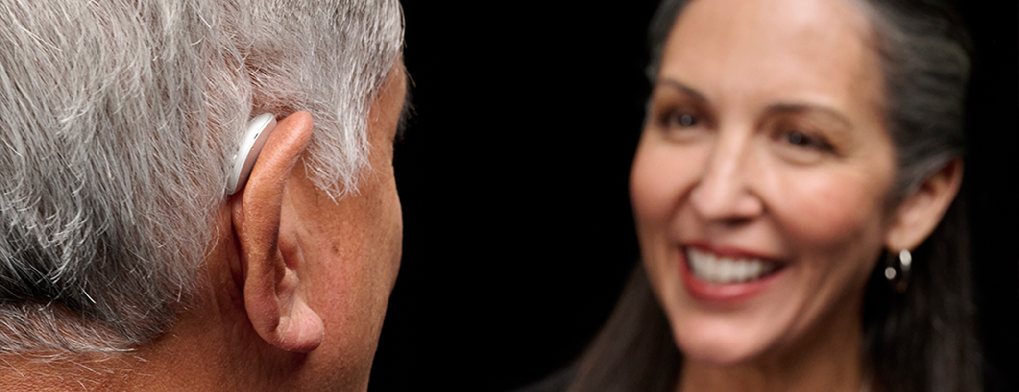Image of a middle aged male wearing an Omega AI Plus hearing aid and chatting to a middle aged female